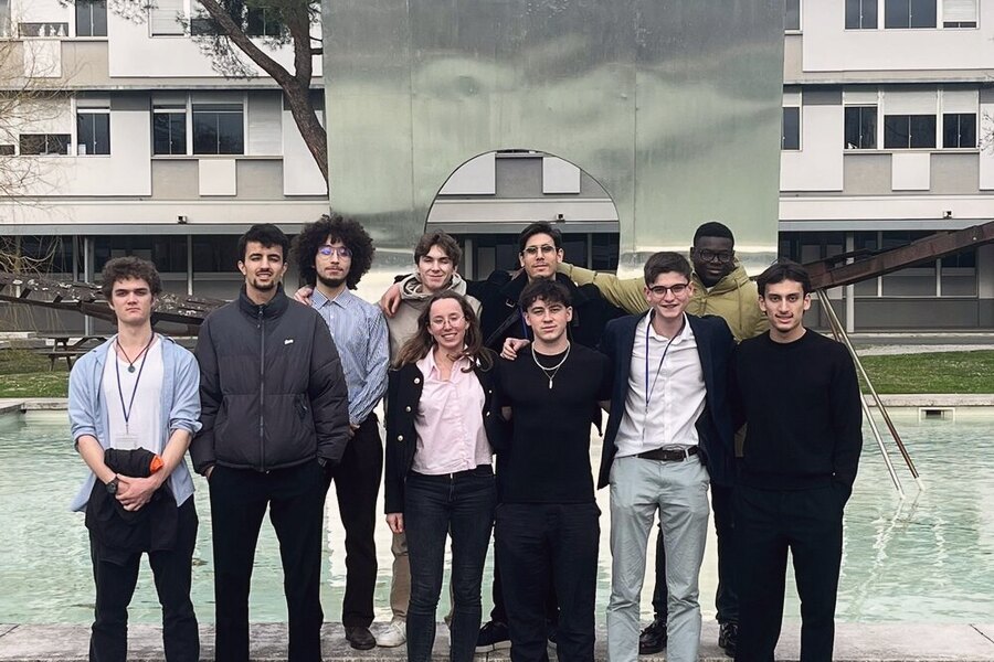 Une dizaine de personnes debout en extérieur devant un bâtiment vitré, plan d'eau au premier plan.