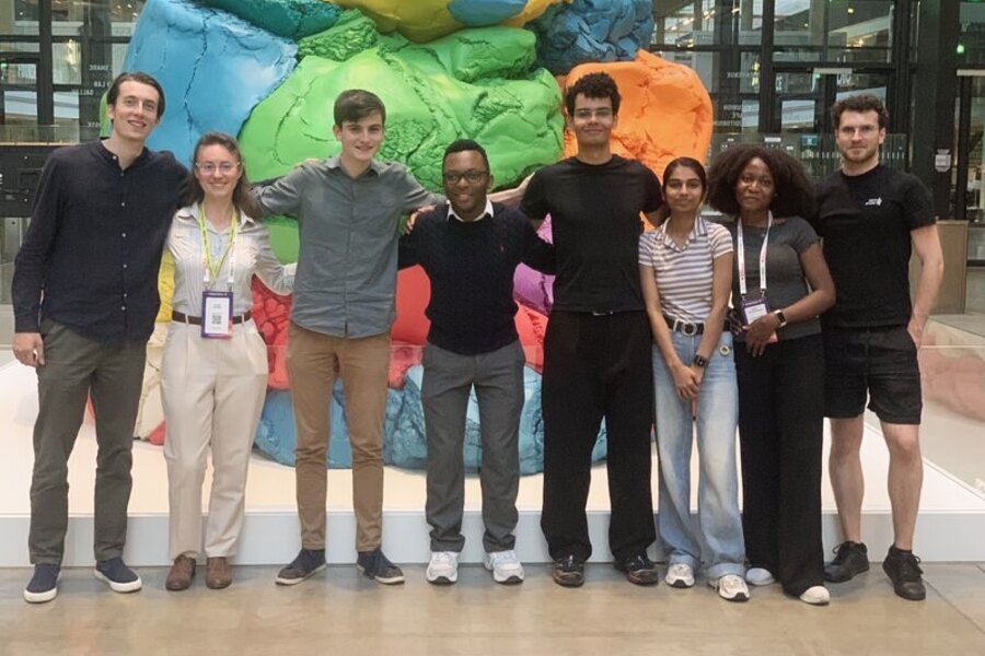 Une dizaine de personnes en extérieur devant une sculpture colorée, plusieurs tiennent un trophée.